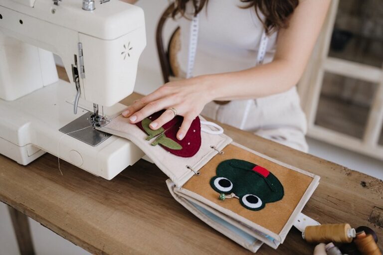 Varrónő kézzel varrt textil csendeskönyvet készít varrógépen, epres és békás foglalkoztató oldalakkal